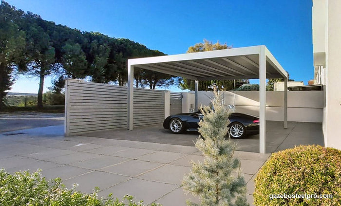 Pergola QBox Linea bianca usata come posto auto, con un'auto nera sotto e una recinzione a doghe