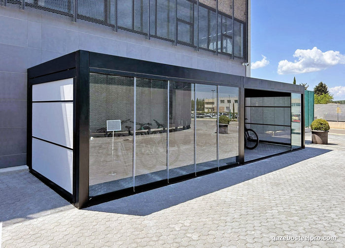 Pergola QBox Linea nera a due moduli in fila davanti a un edificio, chiusa con vetrate scorrevoli e pannelli bianchi
