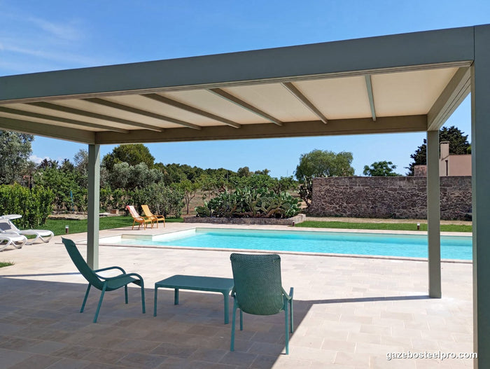 Sotto la pergola QBox Linea verde salvia: copertura in PVC beige tesa fra le traverse, trave alta e piscina dietro